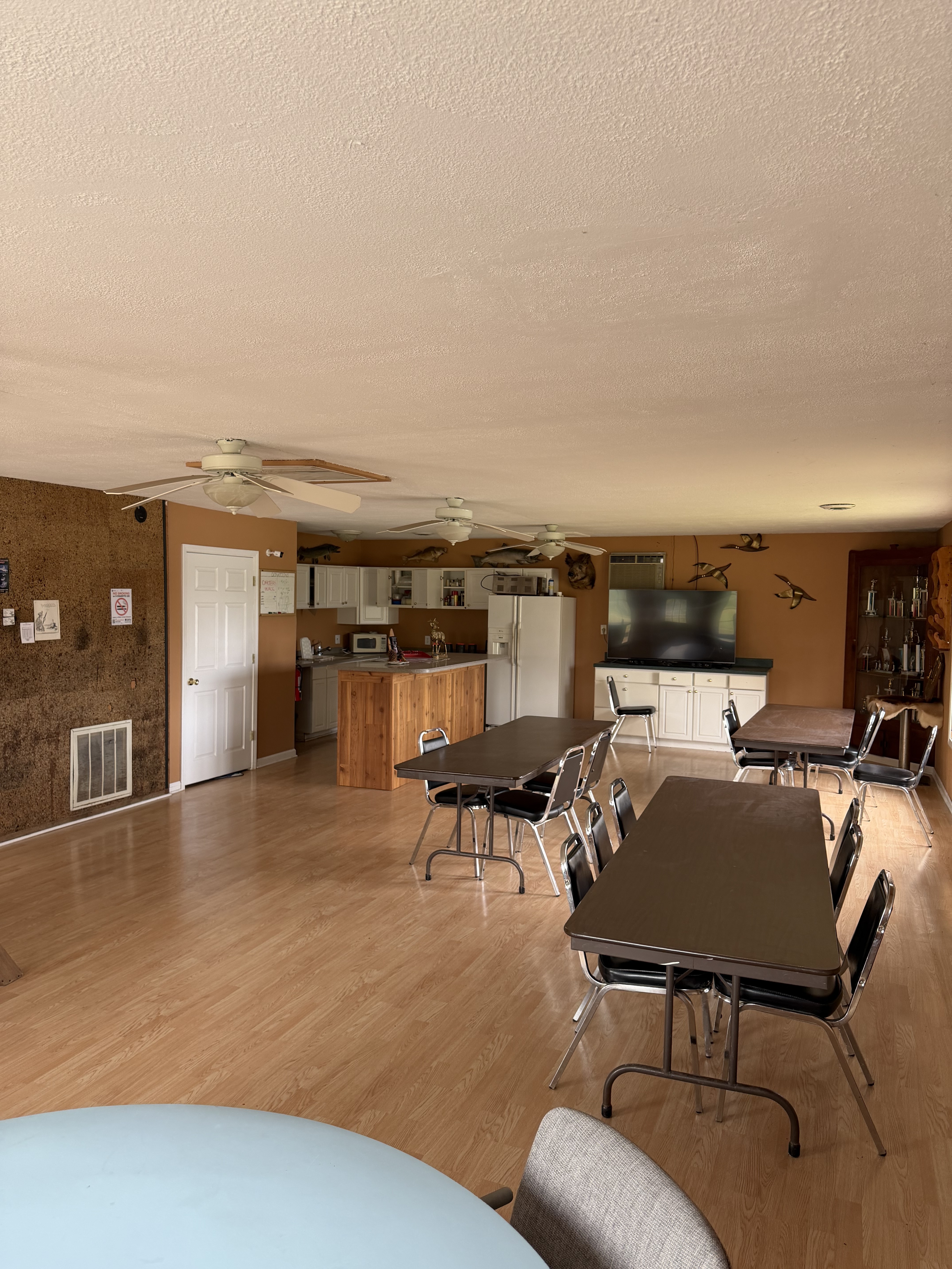 Wide view of the Deer Creek Recreation Club Trap House interior showing dining tables, kitchen area, flat screen TV, and trophy fish mounts