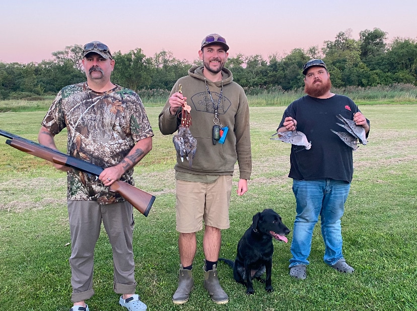 Three hunters with harvested waterfowl and a hunting dog after a successful hunt at Deer Creek Recreation Club